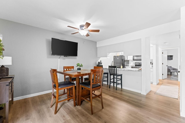 dining space with baseboards, light wood finished floors, and ceiling fan