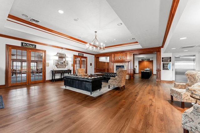 living room with baseboards, ornamental molding, wood-type flooring, a chandelier, and a raised ceiling