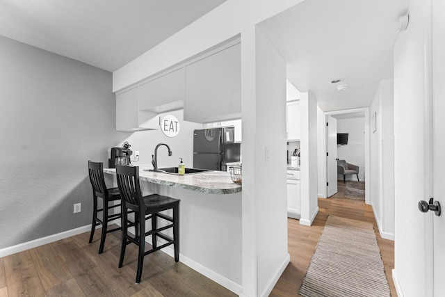 kitchen with freestanding refrigerator, light countertops, a sink, and wood finished floors
