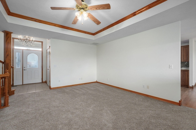 empty room featuring crown molding, a raised ceiling, baseboards, and light colored carpet