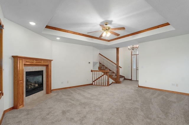 unfurnished living room with stairs, light carpet, a raised ceiling, a tiled fireplace, and ceiling fan with notable chandelier