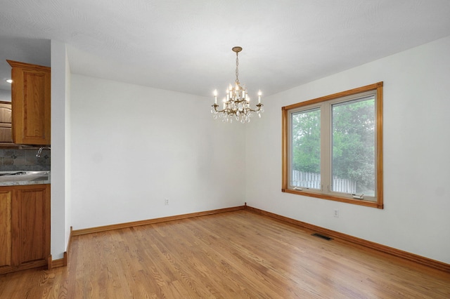 unfurnished dining area with visible vents, light wood-type flooring, a sink, baseboards, and an inviting chandelier