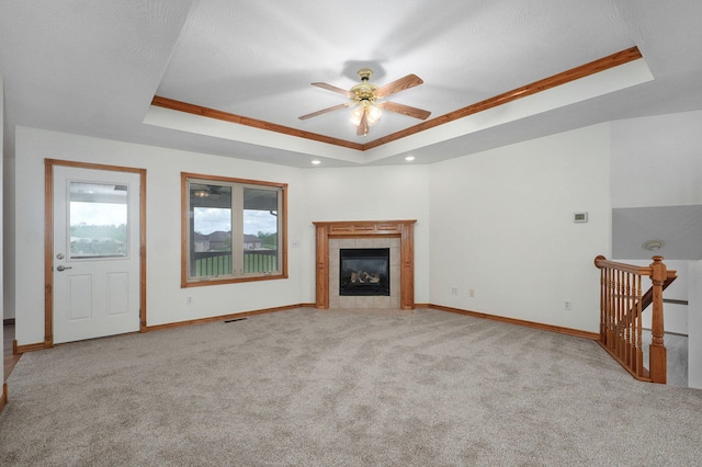 unfurnished living room with a ceiling fan, a tiled fireplace, a raised ceiling, baseboards, and carpet floors