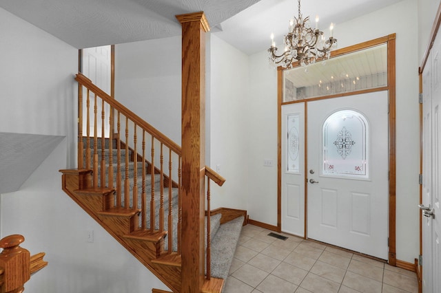 foyer entrance with visible vents, light tile patterned floors, baseboards, an inviting chandelier, and stairs