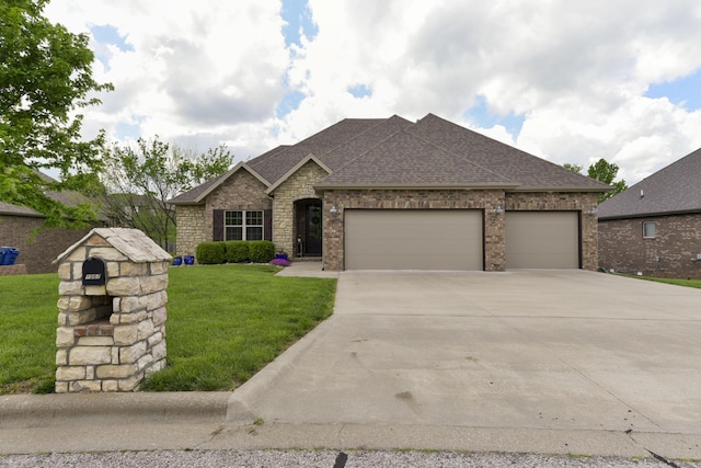 view of front of home with a shingled roof, an attached garage, stone siding, a front yard, and driveway