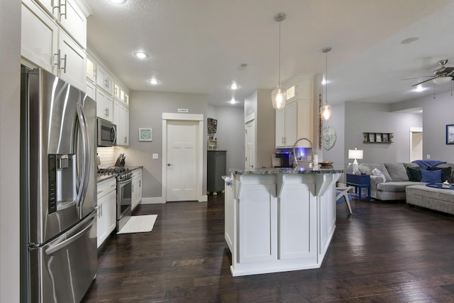 kitchen featuring appliances with stainless steel finishes, a peninsula, open floor plan, stone counters, and white cabinetry