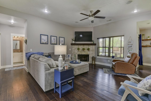 living area with baseboards, ceiling fan, dark wood-style flooring, and a stone fireplace