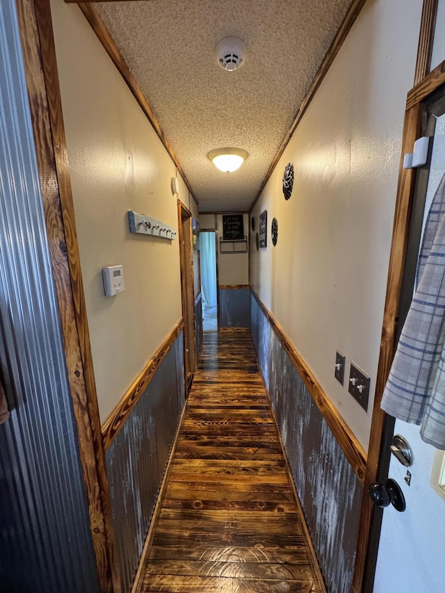 hallway featuring crown molding, a wainscoted wall, dark wood-style floors, and a textured ceiling