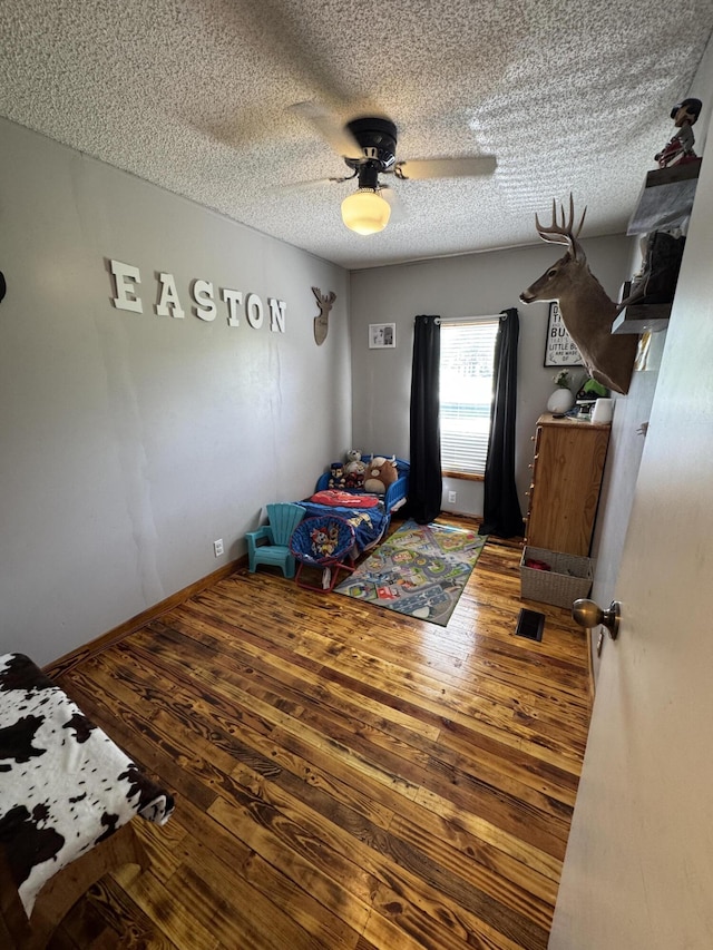 bedroom with baseboards, a textured ceiling, ceiling fan, and hardwood / wood-style flooring