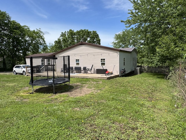 back of property featuring a wooden deck, fence, a trampoline, and a lawn