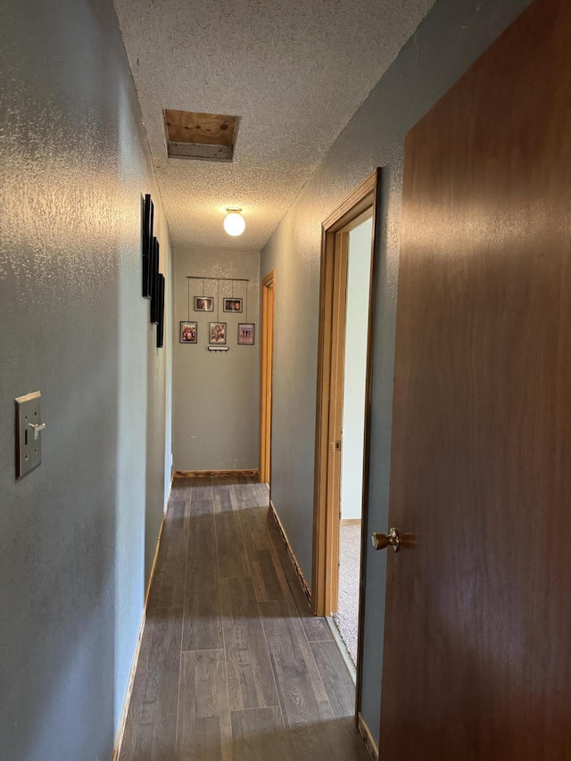 hall with attic access, a textured ceiling, visible vents, baseboards, and dark wood-style floors