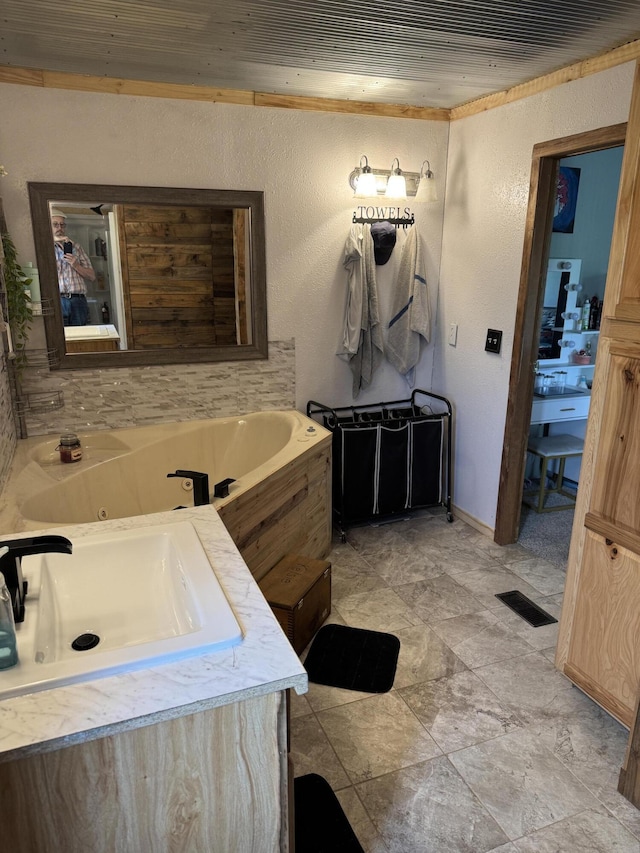 full bath with a tub with jets, a sink, a textured wall, and visible vents