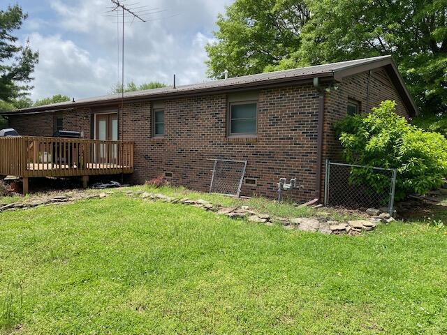 rear view of property with a yard, a deck, brick siding, and fence