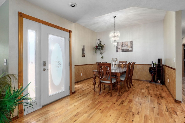 dining area featuring light wood-style flooring, a chandelier, and a wainscoted wall