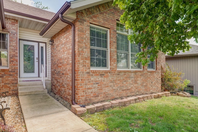 entrance to property featuring brick siding and a lawn