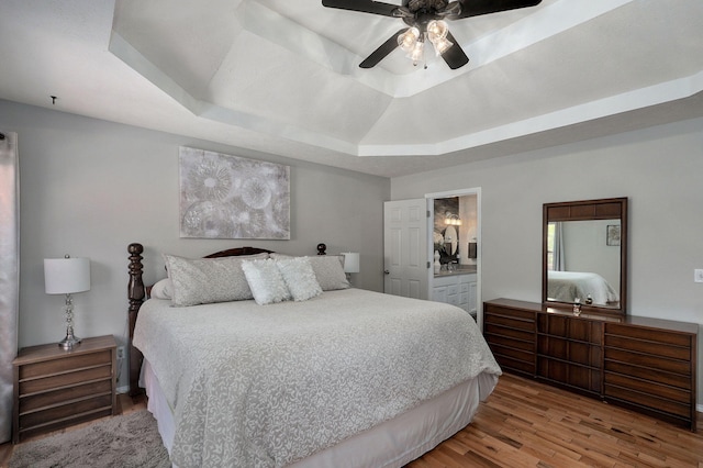 bedroom featuring a tray ceiling, ceiling fan, ensuite bath, and wood finished floors
