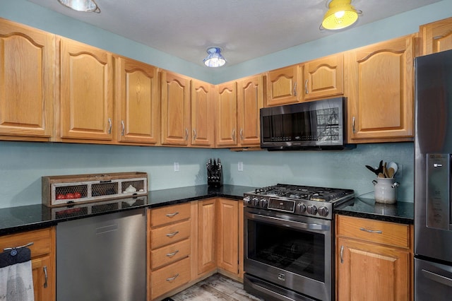 kitchen featuring stainless steel appliances, dark stone countertops, and light wood-style flooring