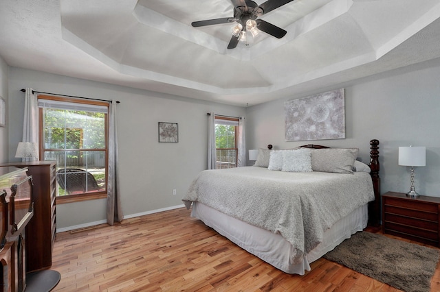 bedroom featuring baseboards, ceiling fan, a tray ceiling, and light wood-type flooring