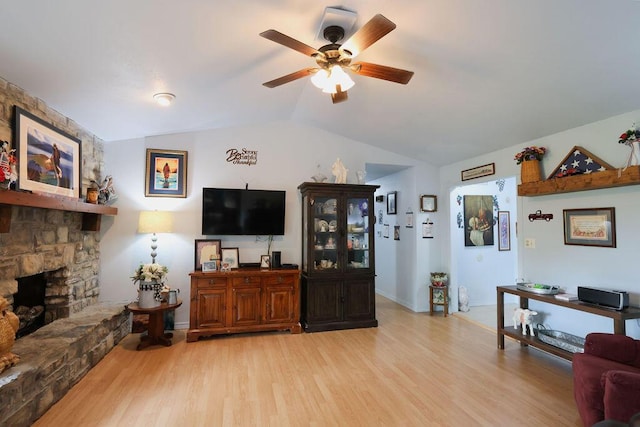 living room with baseboards, a stone fireplace, light wood finished floors, ceiling fan, and vaulted ceiling