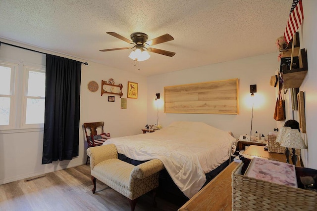 bedroom featuring wood finished floors, a textured ceiling, visible vents, a ceiling fan, and baseboards