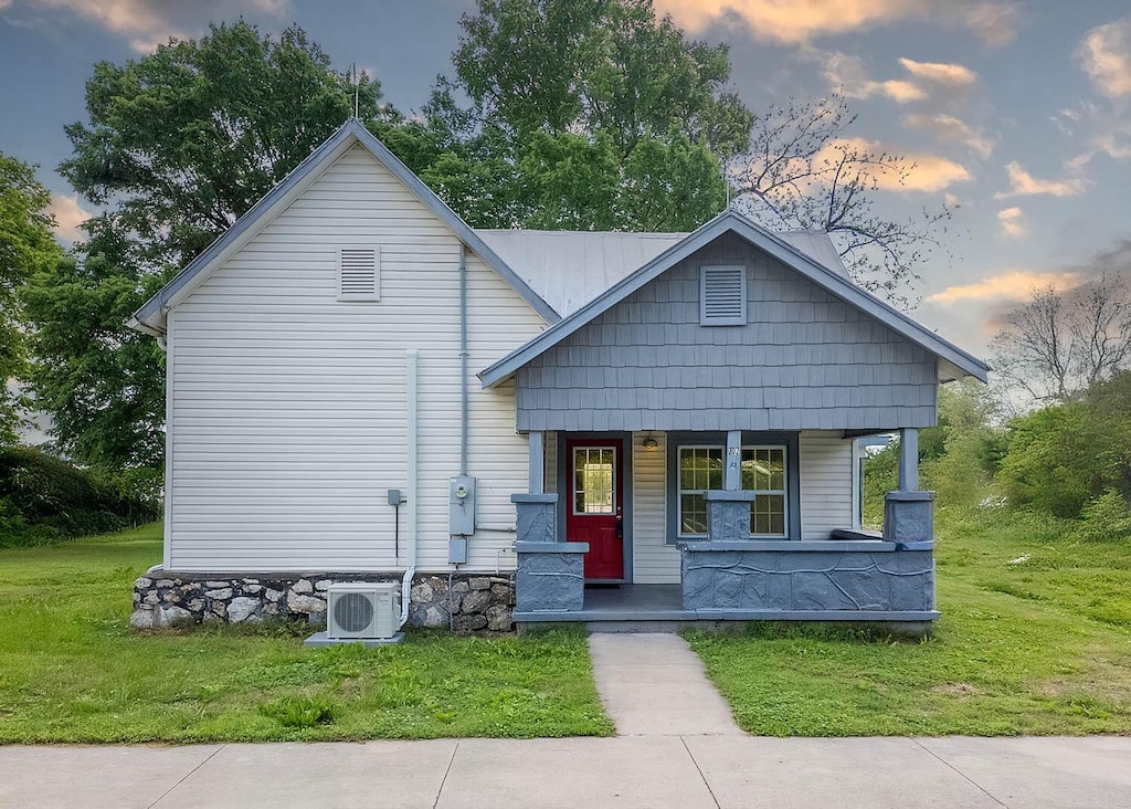 bungalow-style home with ac unit, a porch, and a lawn