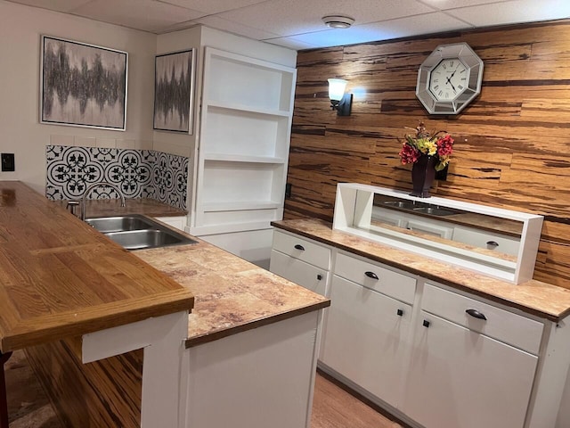 kitchen featuring a drop ceiling, a sink, open shelves, white cabinetry, and light countertops