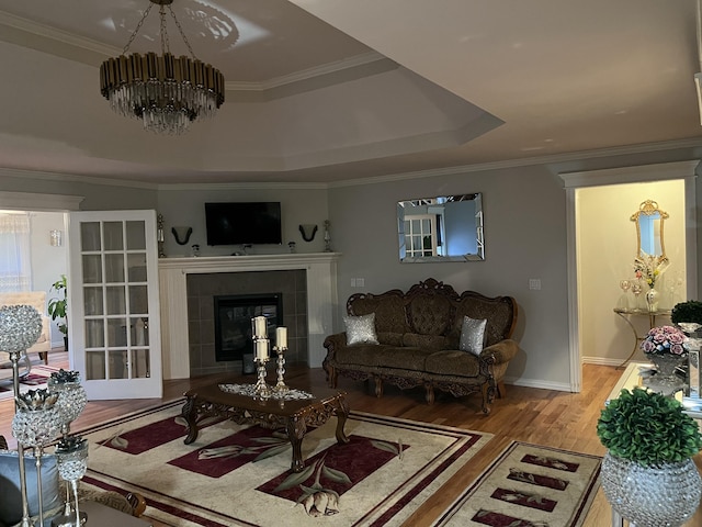 living area featuring wood finished floors, ornamental molding, a fireplace, a raised ceiling, and a notable chandelier