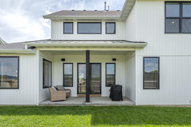 back of house with a yard, a standing seam roof, metal roof, a patio, and a shingled roof