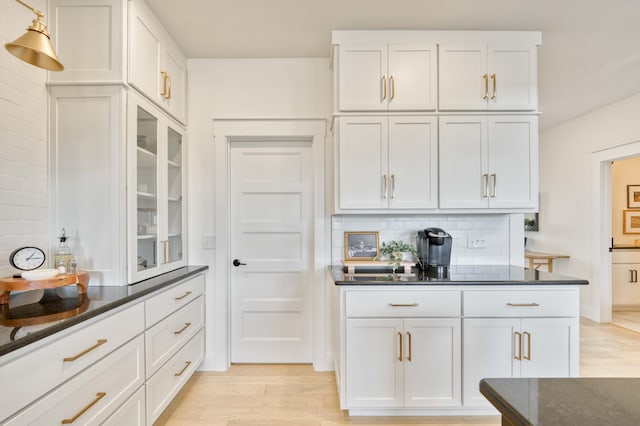 kitchen featuring light wood finished floors, glass insert cabinets, dark stone counters, white cabinetry, and backsplash