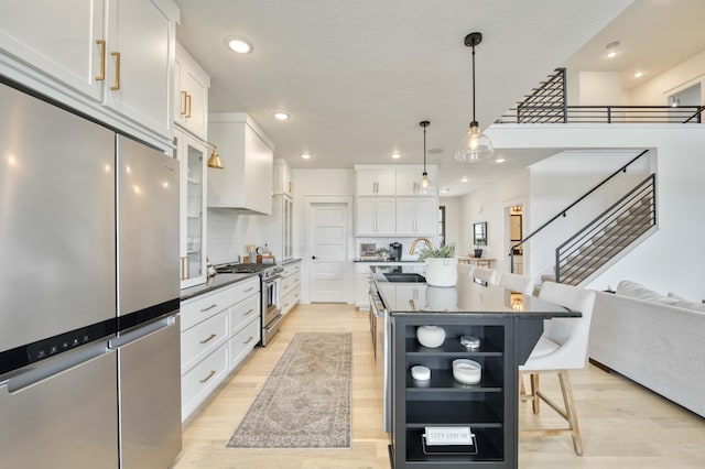 kitchen with a kitchen bar, white cabinetry, dark countertops, stainless steel appliances, and light wood-type flooring