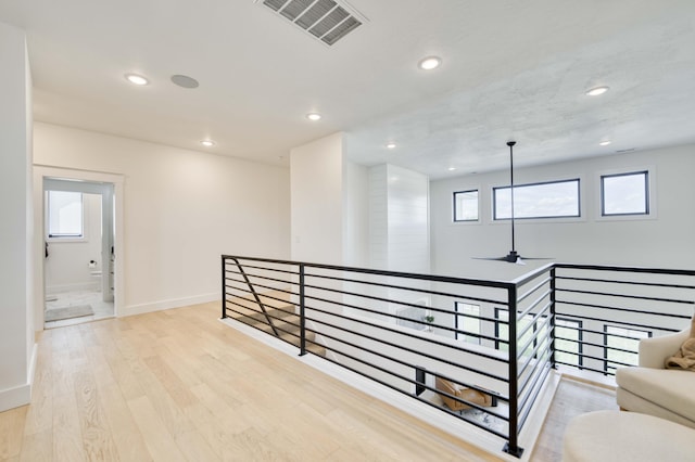 hall with light wood-style flooring, recessed lighting, baseboards, visible vents, and an upstairs landing