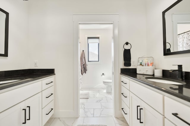 bathroom featuring baseboards, marble finish floor, two vanities, and a sink