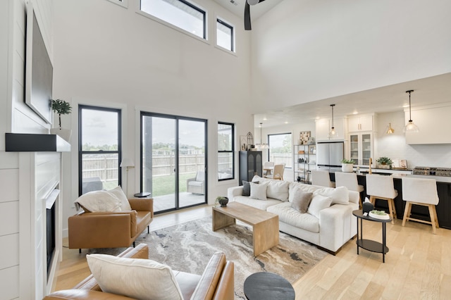 living area featuring a fireplace, light wood-type flooring, and a high ceiling