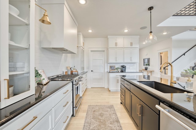 kitchen with a sink, stainless steel appliances, white cabinetry, and decorative light fixtures