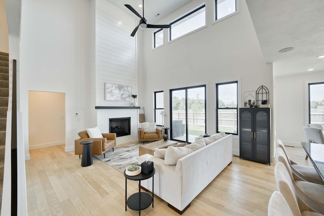 living room featuring a large fireplace, light wood-style flooring, ceiling fan, and a high ceiling