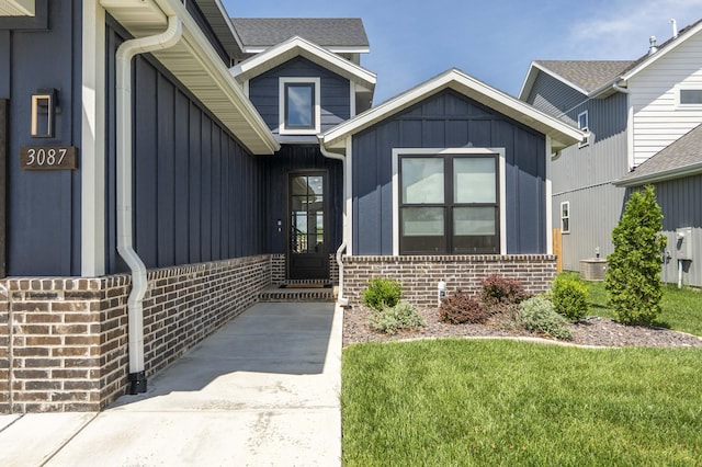 doorway to property with board and batten siding, brick siding, and a lawn