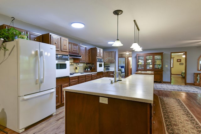 kitchen featuring light countertops, light wood-type flooring, a center island with sink, and white appliances