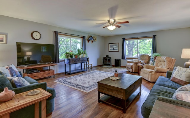 living room with a ceiling fan, a wood stove, a healthy amount of sunlight, and wood finished floors