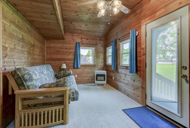 sitting room featuring heating unit, carpet, a ceiling fan, wooden ceiling, and wooden walls