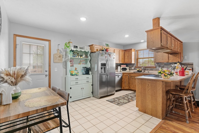 kitchen featuring a peninsula, a sink, backsplash, light countertops, and appliances with stainless steel finishes
