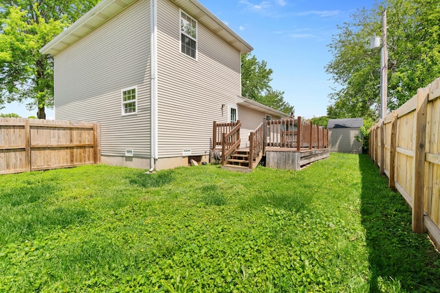 exterior space featuring a storage shed, a deck, a lawn, a fenced backyard, and an outbuilding