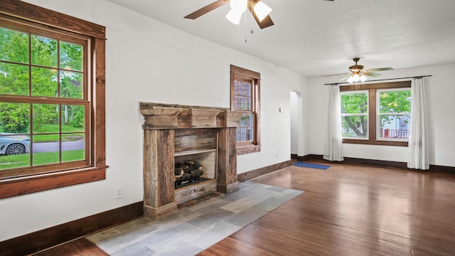 unfurnished living room with a fireplace with flush hearth, arched walkways, a ceiling fan, and baseboards