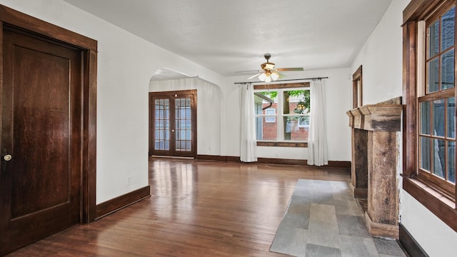 unfurnished living room featuring ceiling fan, arched walkways, baseboards, and wood finished floors