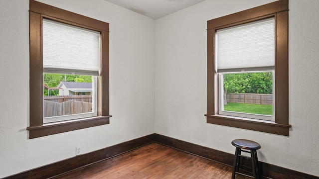 empty room featuring baseboards, dark wood-style flooring, and a wealth of natural light