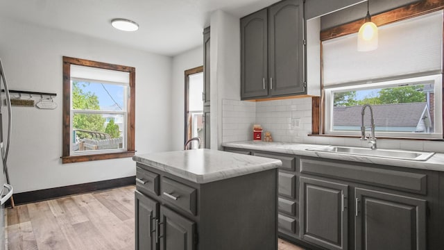 kitchen featuring baseboards, a sink, a kitchen island, backsplash, and light wood-style floors