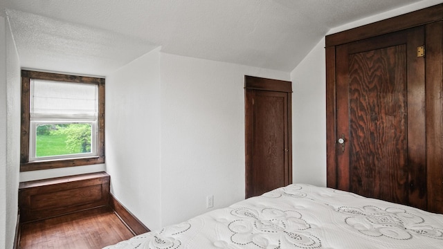 bedroom featuring lofted ceiling, a textured ceiling, baseboards, and wood finished floors