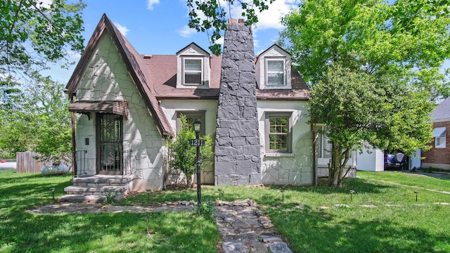 view of front facade with stone siding, fence, a chimney, and a front yard
