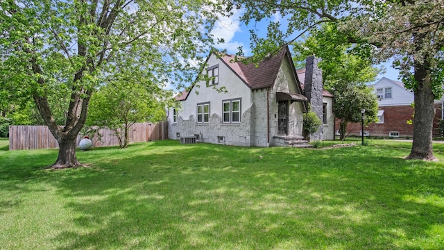 exterior space featuring fence, central AC, stucco siding, a front yard, and a chimney