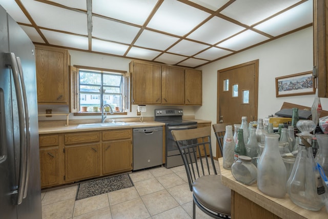 kitchen featuring brown cabinetry, light tile patterned floors, a sink, light countertops, and appliances with stainless steel finishes