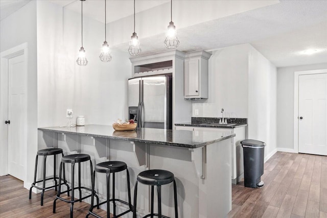 kitchen with stainless steel fridge, a breakfast bar area, a sink, and wood finished floors